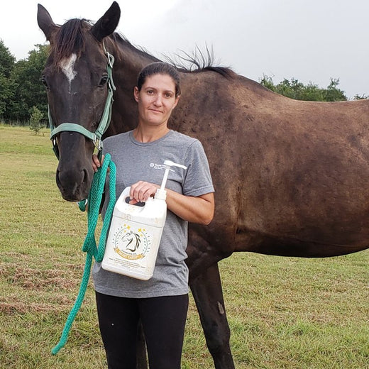 Candice M. in the field beside her Thoroughbred gelding, holding a jug